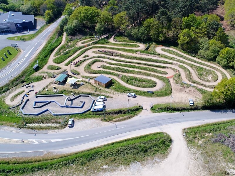 Vue aérienne d'un circuit de quad avec plusieurs pistes sinueuses entourées d'arbres et de bâtiments.