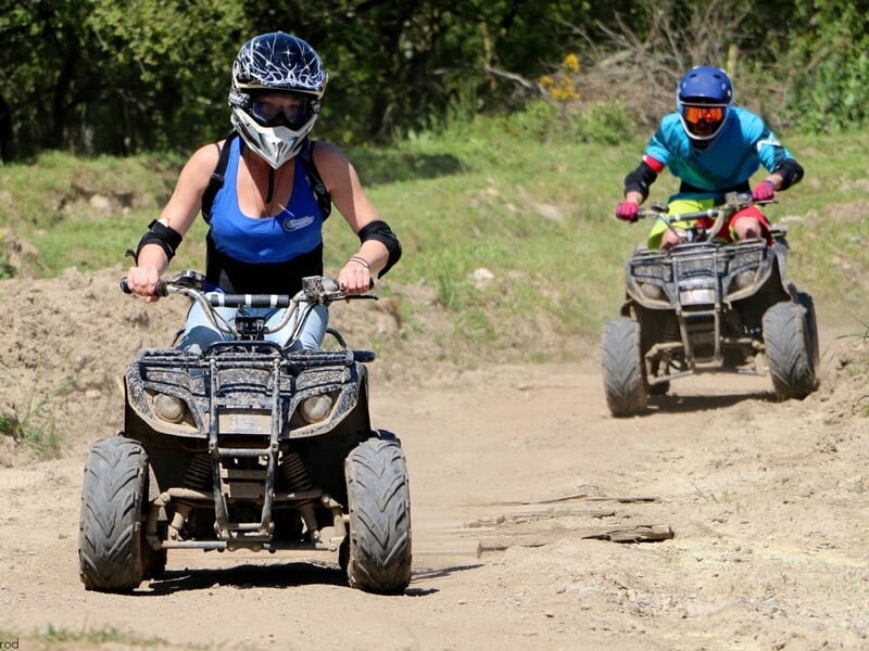 Deux personnes en tenue de protection conduisant des quads sur un chemin de terre dans un environnement naturel.