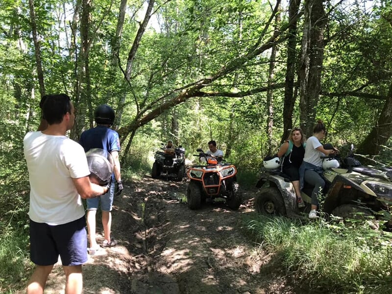 Groupe de personnes en quad traversant un sentier forestier avec des spectateurs debout sur le côté.