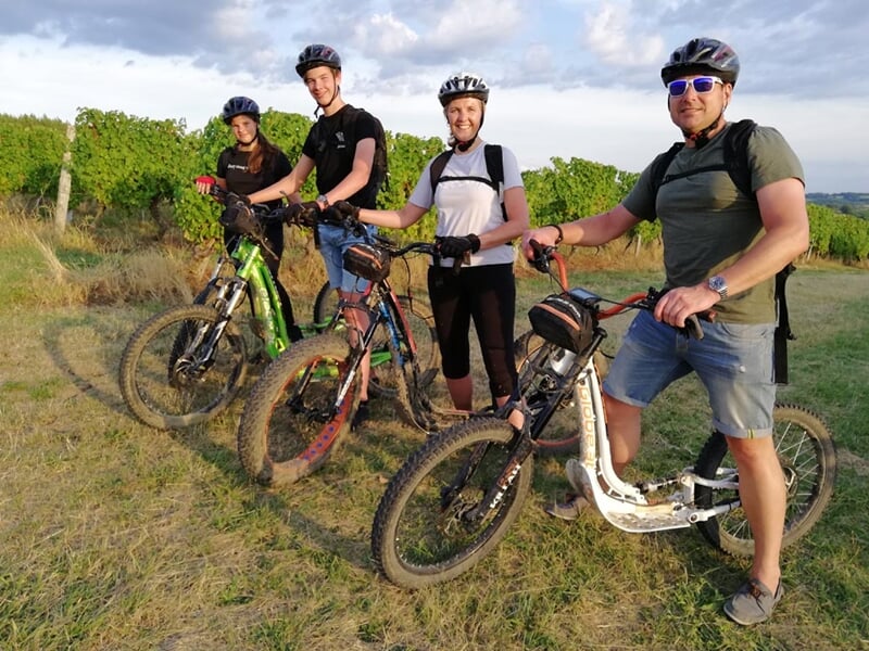 Quatre personnes debout avec des vélos électriques sur un chemin herbeux au coucher du soleil.