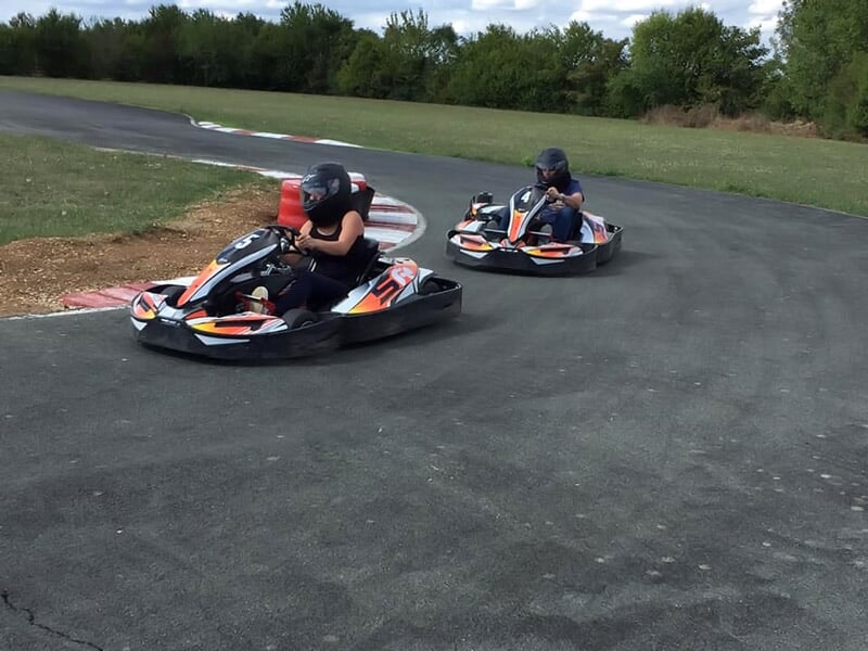 Deux jeunes pilotes en casque conduisent leurs karts sur une piste de karting entourée d'herbe verte.