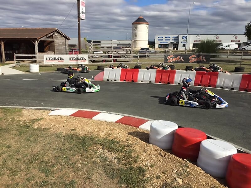 Deux karts en course sur une piste avec des barrières rouges et blanches, sous un ciel partiellement nuageux.