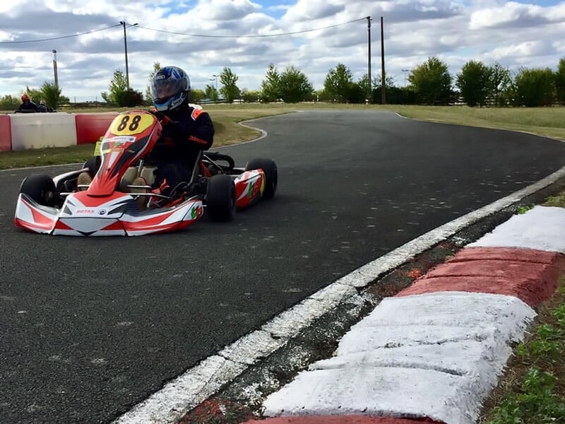 Un pilote en kart rouge numéro 88 roule sur une piste de karting avec des bordures rouges et blanches.