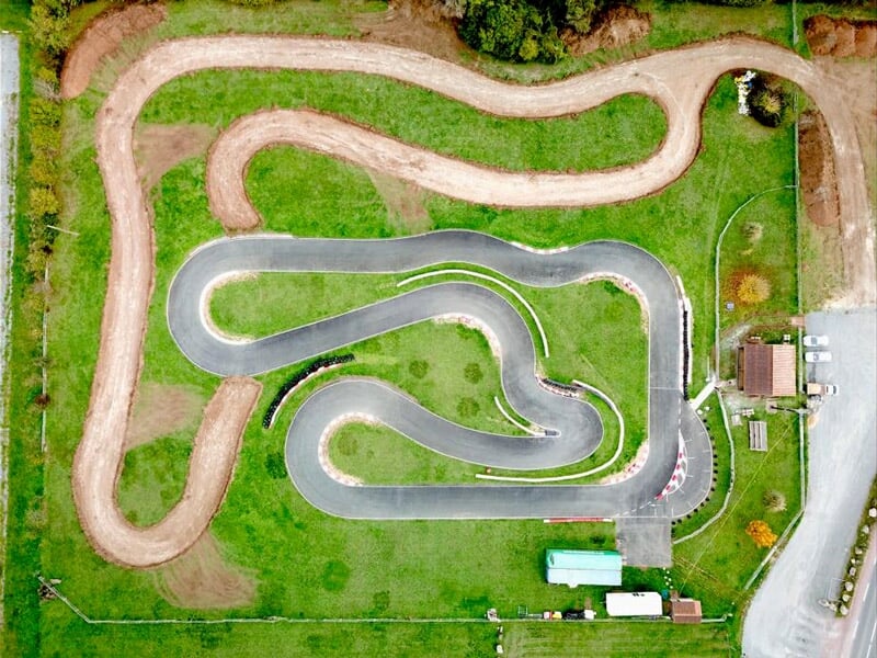 Vue aérienne d'un circuit de karting avec plusieurs virages serrés et une zone de pelouse autour.