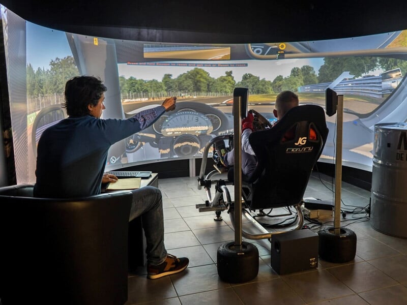 Deux personnes utilisent un simulateur de conduite automobile avec un grand écran panoramique à Mérignac.