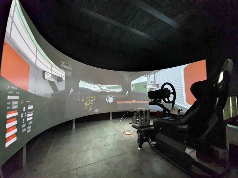 Simulateur de conduite automobile avec siège et volant devant un écran incurvé affichant une route virtuelle.