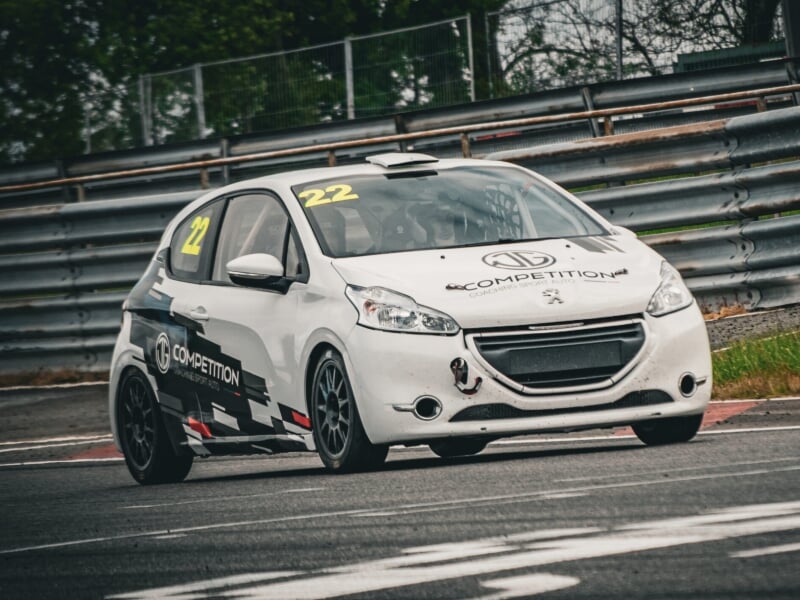 Véhicule de course blanc avec marquages noirs et jaunes portant le numéro 22 en pleine action sur un circuit, barrières de sécurité en arrière-plan.