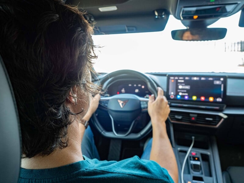 Vue intérieure d'un véhicule électrique moderne avec un conducteur concentré sur l'écran tactile du tableau de bord, des touches de couleur bleu canard sur le siège et la tenue du conducteur.