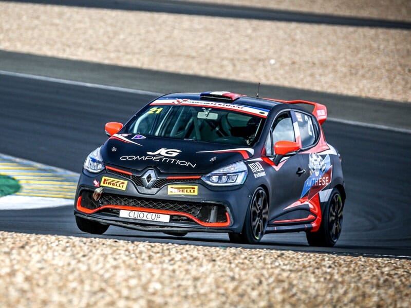 Renault Clio de course noire et rouge en pleine action sur un circuit, pneus Pirelli, inscriptions 