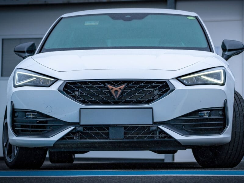 Gros plan de l'avant d'une Cupra blanche, phares allumés, grille avant distinctive.