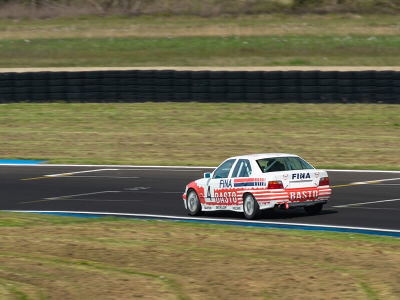 BMW Basto rouge et blanc vue arrière sur piste de course entourée d'herbe et barrières de sécurité.