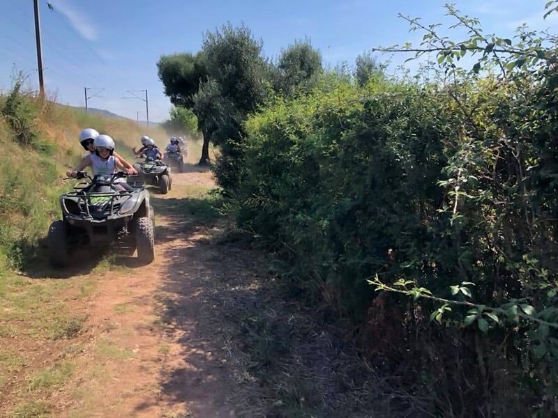 Quads en file indienne sur un chemin étroit bordé de buissons et d'arbustes verts sous un ciel bleu.