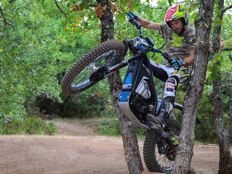 Un pilote en tenue complète effectue un saut spectaculaire en VTT électrique dans un sentier forestier en Vaucluse.