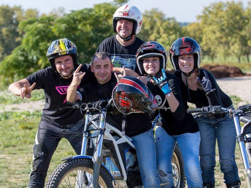 Groupe de cinq personnes souriantes avec casques posant avec leurs VTT électriques sur un terrain dégagé en plein air.