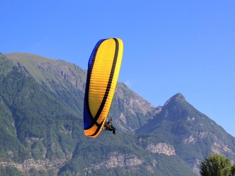 Un paramoteur jaune et noir vole devant une montagne sous un ciel bleu clair sans nuages.