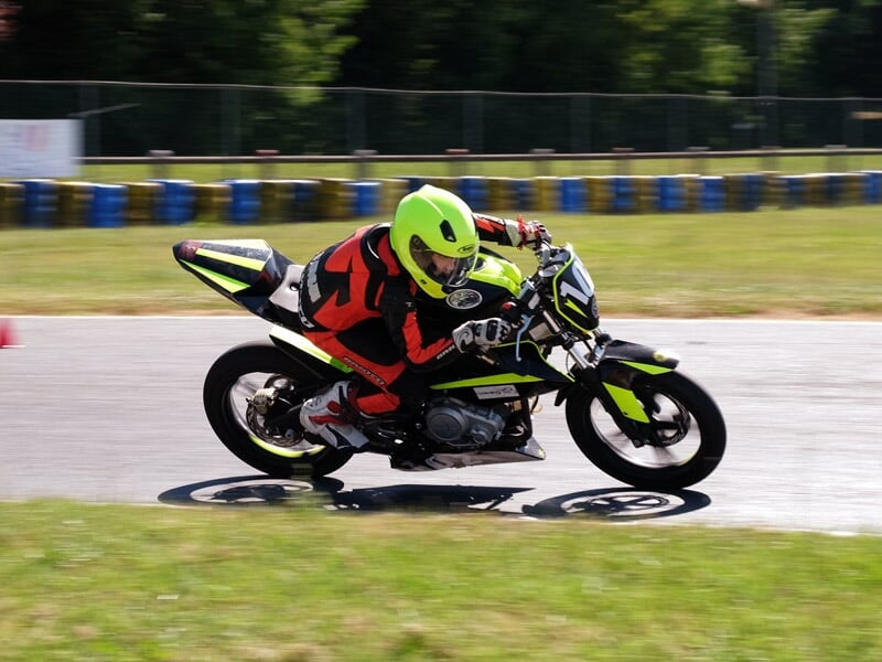 Motard en tenue rouge et casque jaune fluo en pleine accélération sur une piste de course avec barrières bleues.