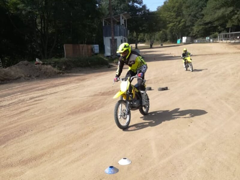 Des apprentis pilotes font des exercices de mobilité entre des cônes sur une piste de motocross