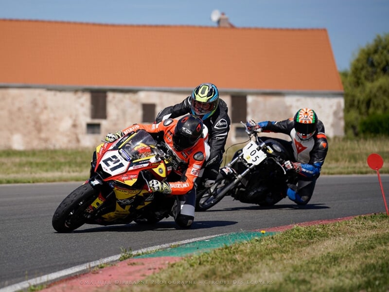deux motos dont celle au premier plan comprend deux personnes dessus roulent sur un circuit