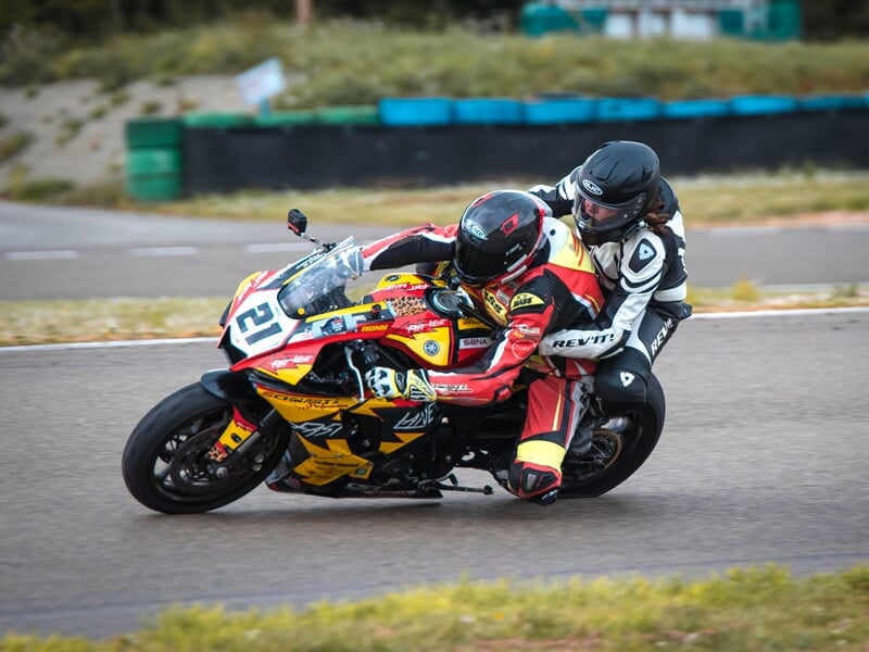 une moto avec deux personnes dessus équipées de casques en plein virage sur un circuit