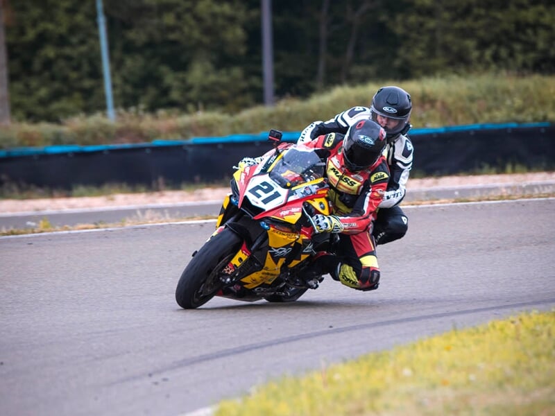 deux personnes sur une moto de course roulent sur un circuit asphalte