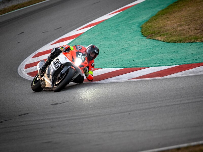 Un pilote de moto en tenue de course rouge et noire incliné sur une moto sportive pendant un virage sur circuit