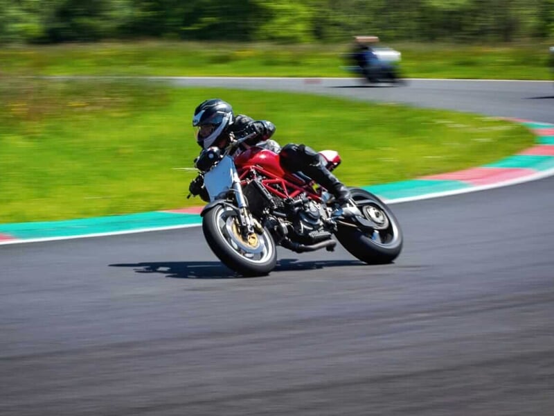 Un pilote en combinaison de course noire et rouge sur une moto rouge dans un virage rapide sur piste