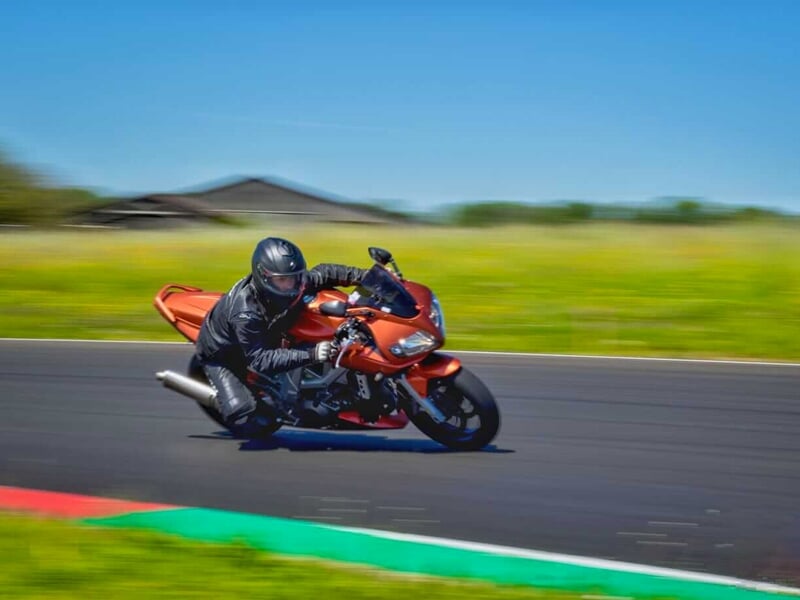 un pilote de moto habillé en noir sur une moto orange en plein virage sur un circuit