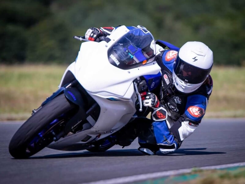 Un pilote de moto penché dans un virage serré sur une moto sportive blanche et bleue sur un circuit de course