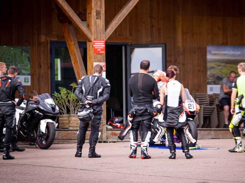 Des pilotes de course de moto en combinaison protectrice se tenant près d'une cabane en bois sur un circuit