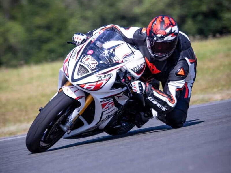 Un pilote de moto en combinaison orange et noire effectuant un virage à grande vitesse sur une moto de course Triumph