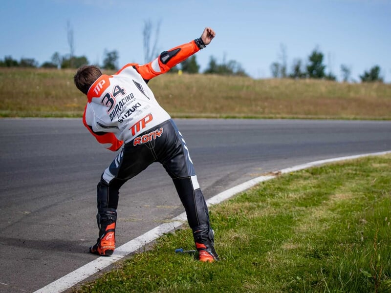 Un pilote en combinaison de course orange s'étirant sur le bord d'une piste de course