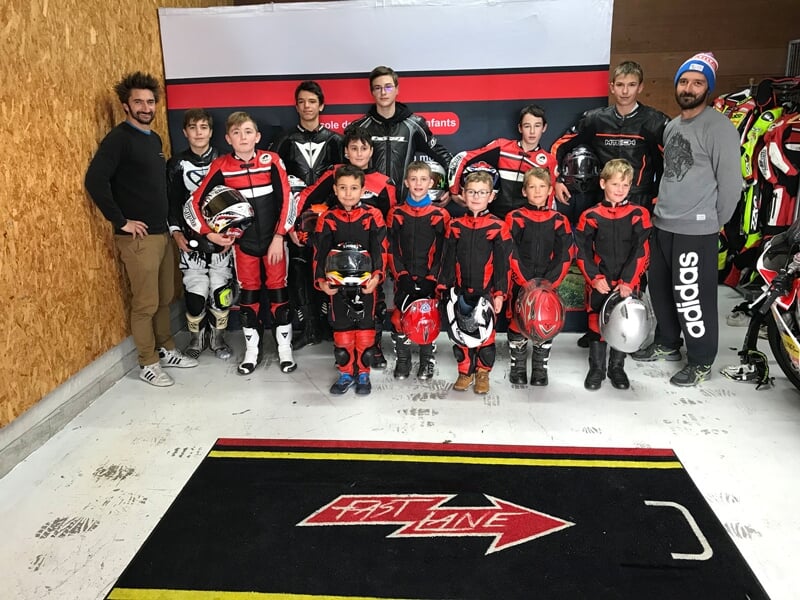 un groupe d'enfants pose en combinaison noir et rouge avec des moniteurs de moto