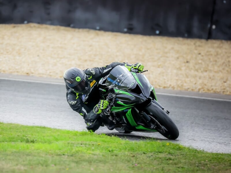 un pilote de moto sportive en combinaison noire et verte en plein virage dans un circuit