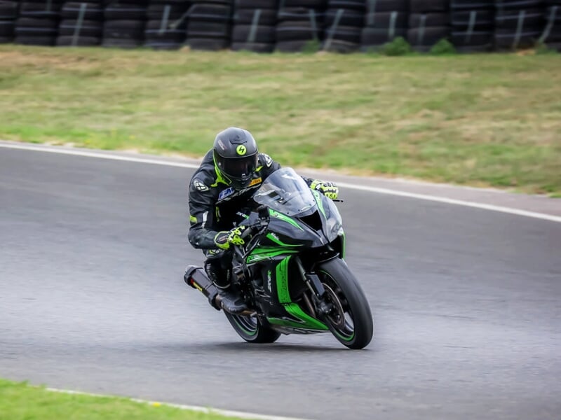 Un pilote en combinaison noire et verte roule à grande vitesse sur une moto sportive noire et verte sur une piste de course.