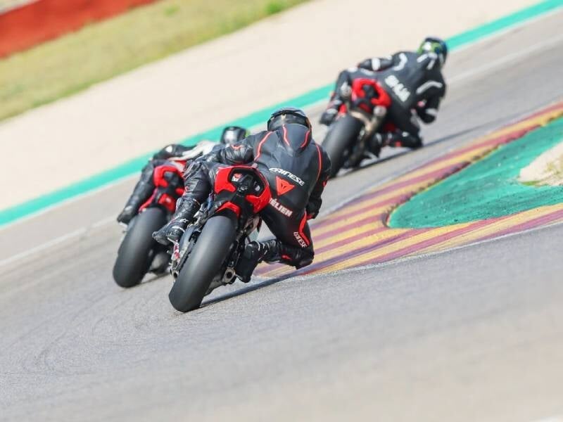 Trois motards en tenue noire et rouge pilotent leurs motos sportives sur un circuit en virage serré, concentrés.