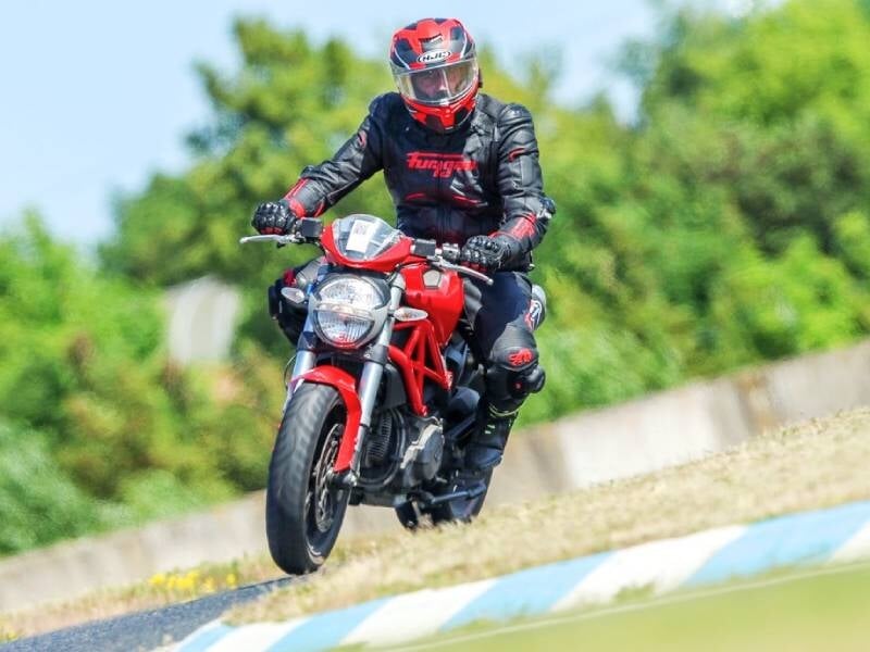 Pilote en tenue complète et casque rouge conduisant une moto rouge sur un circuit avec un fond de verdure floue.