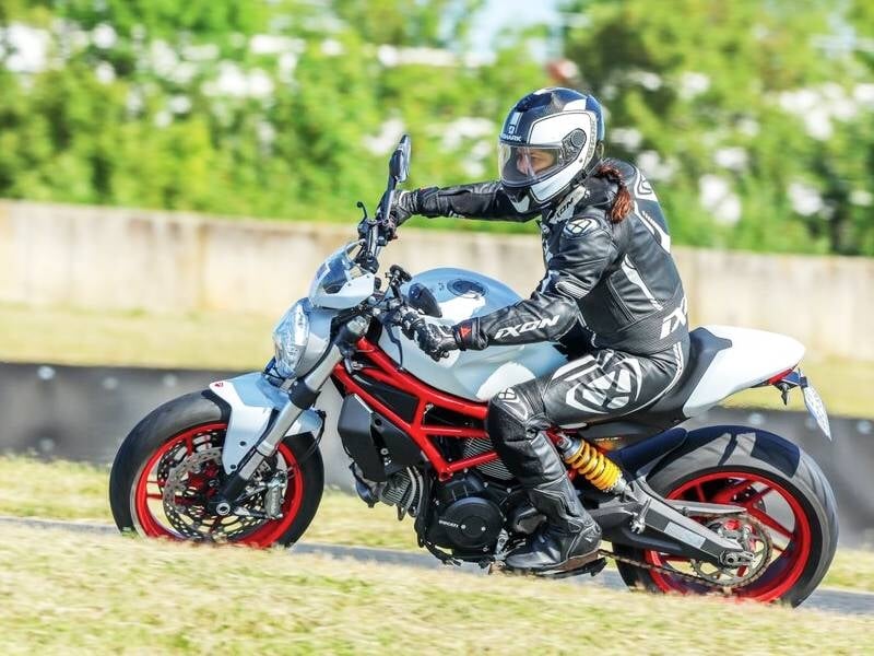 Femme en tenue de moto complète sur une moto sportive blanche et rouge sur circuit avec fond flou vert.