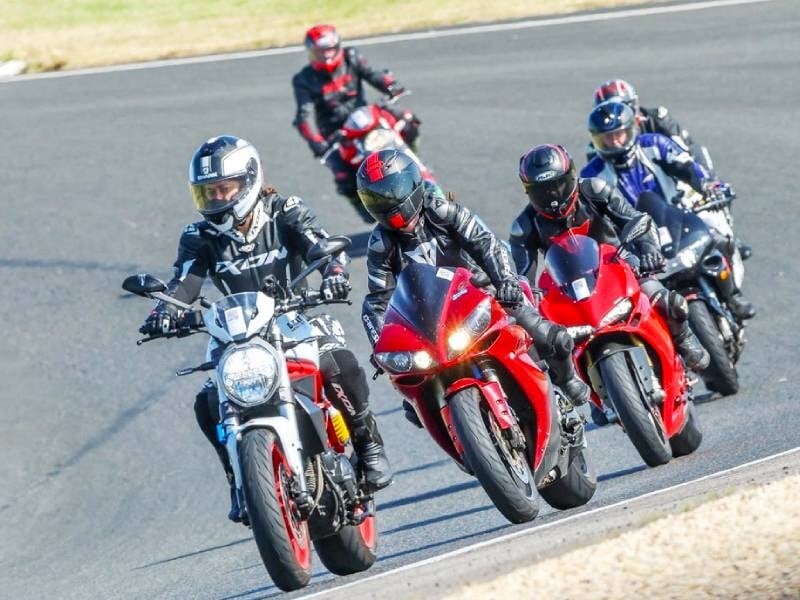 Cinq motards en tenue complète pilotent leurs motos sportives sur un circuit lors d'un stage de pilotage moto.