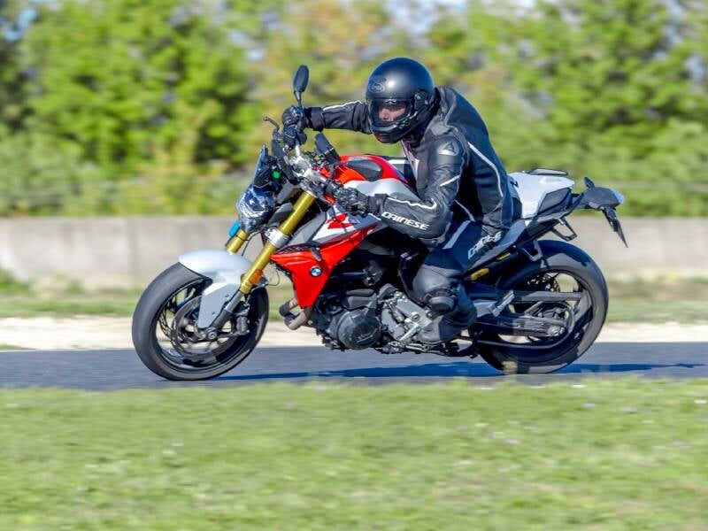 Motard en tenue complète et casque noir pilotant une moto sportive rouge et blanche sur circuit en virage.