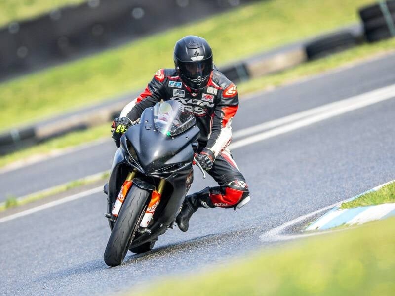 Pilote en combinaison noire et rouge sur une moto sportive noire prenant un virage sur un circuit asphalté en plein jour