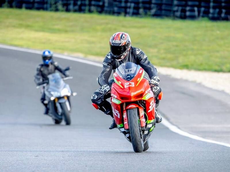 Pilote en combinaison noire sur moto rouge numéro 23 sur circuit, avec un autre motard en arrière-plan sur piste