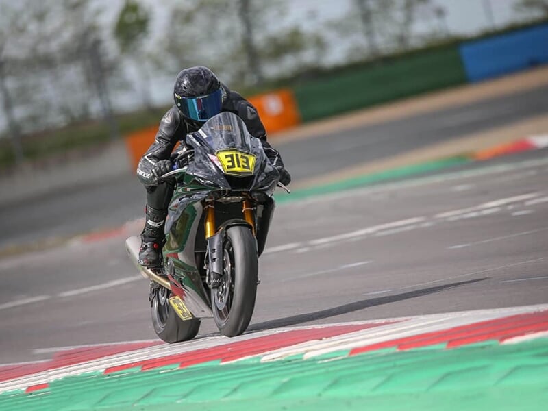 Pilote sur une moto noire numérotée 313, en pleine accélération sur une piste avec des bordures vertes, rouges et blanches.