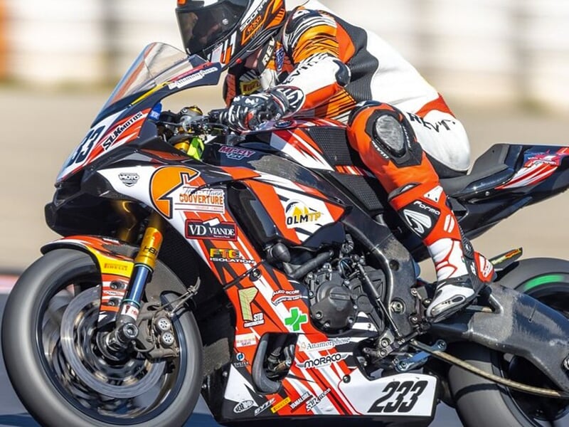Un pilote incliné sur une moto de course orange et blanche numérotée 233, effectuant un virage serré sur circuit.