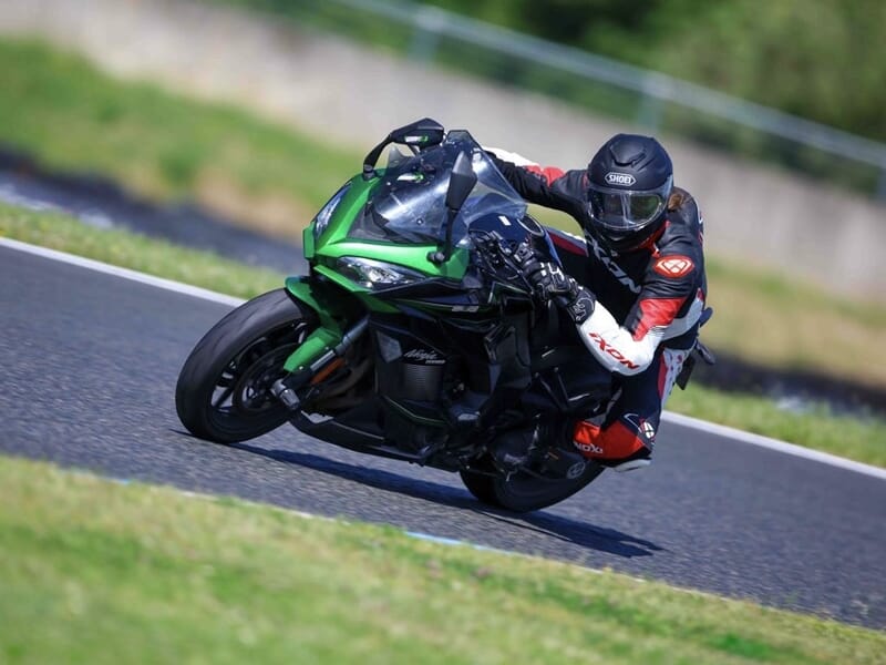 Motard en tenue noire et rouge sur une moto verte, inclinée dans un virage sur piste de course.