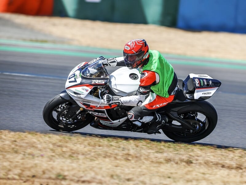 Coureur en combinaison blanche et rouge sur une moto blanche, en pleine accélération sur circuit.