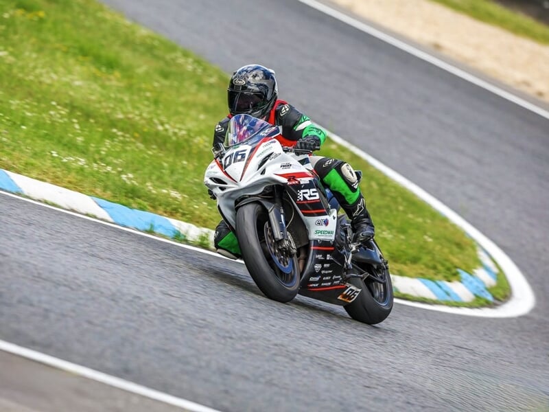 Motard en combinaison verte et noire sur une moto blanche, prenant un virage serré sur piste de course.