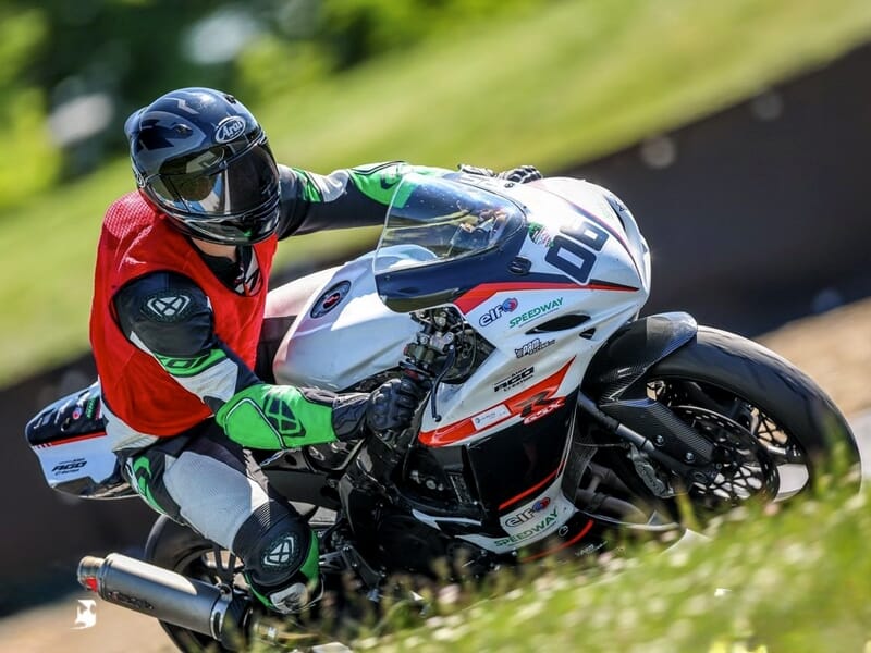 Pilote en tenue rouge et noire sur une moto blanche, concentré en pleine course sur circuit asphalté.