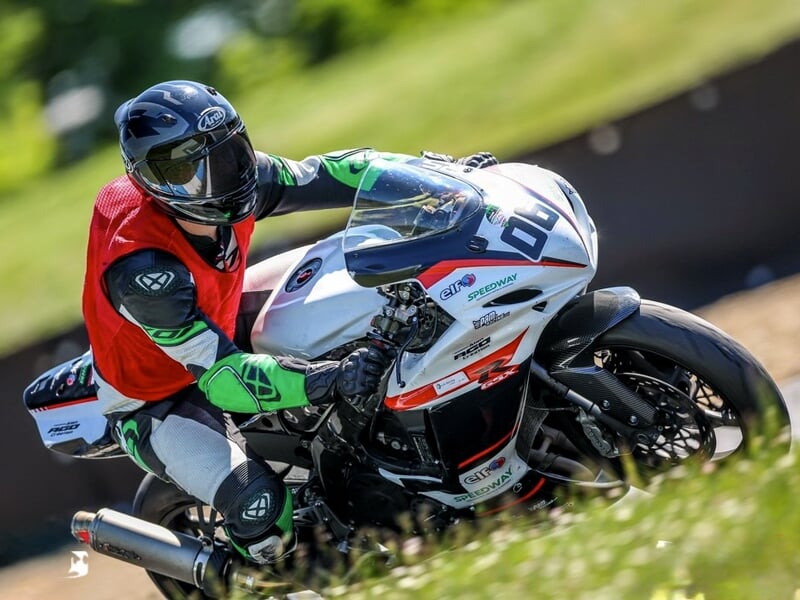Pilote en tenue rouge et noire sur une moto blanche, concentré en pleine course sur circuit asphalté.
