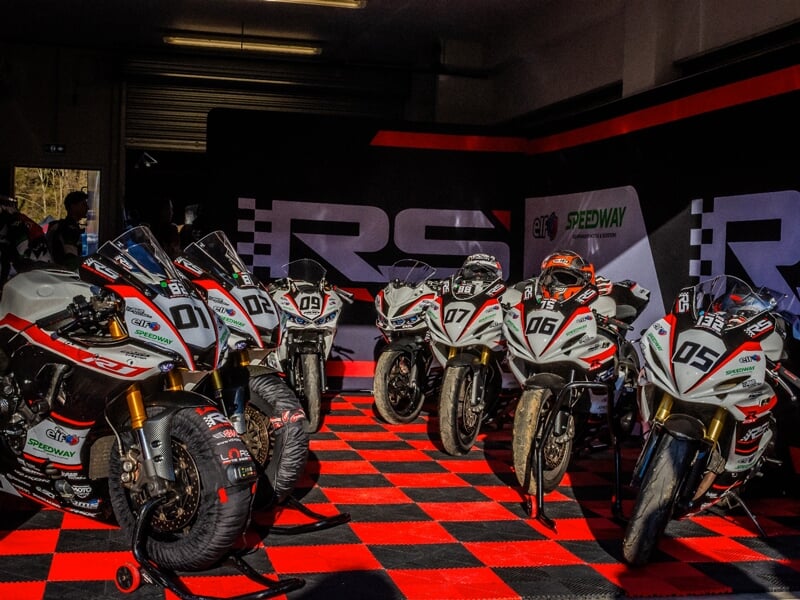 Cinq motos de course blanches alignées dans un garage avec un sol à damier rouge et noir, prêtes à rouler.