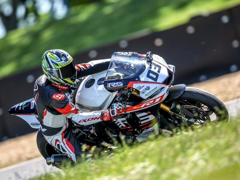 Pilote en combinaison blanche et noire sur une moto blanche, en pleine accélération sur piste de course.